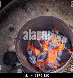 Top-down view of flaming hot charcoal briquettes igniting in a metal grill starter, ready for a barbecue Stock Photo