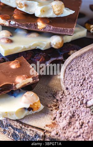 Vertical shot with focus on a ladle with overflowing cocoa. To his left chocolate bars with hazelnuts. Out of focus background and soft side light. Stock Photo