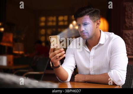 Man unlocking his smartphone with facial recognition app in cafe. Biometric verification Stock Photo