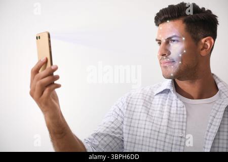 Man unlocking his smartphone with facial scanner against light background. Biometric verification Stock Photo