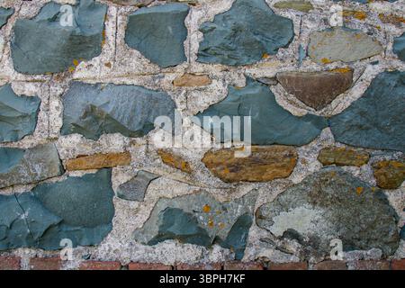 A rustic stone wall showcases an array of textures and colors, featuring smooth and rough surfaces. Stock Photo