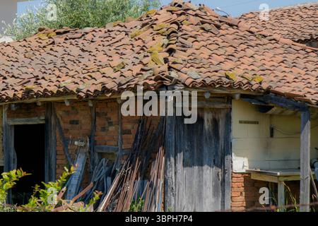 A vintage farmhouse features a distinctively worn roof crafted from terracotta tiles, surrounded by greenery. Stock Photo