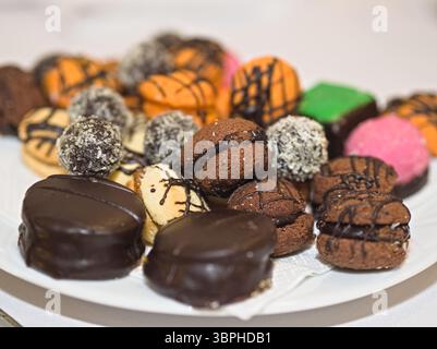 A delightful close-up of a diverse assortment of small pastries and cookies, featuring various colors, toppings, and textures, artfully arranged on a Stock Photo