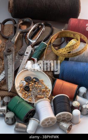 Sewing needles stuck in a green miniature spools thread Steel scissors, Spools of thread of various colour, Thimbles and Measuring tape including Pins Stock Photo