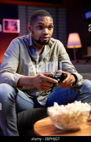Young guy having fun with video games on television modern setup, connecting his console on smart tv in living room and enjoying chill game night at home. African american gamer playing tournament. Stock Photo