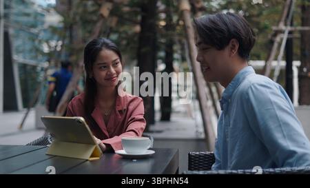 Two young professionals are having a business meeting at an outdoor cafe, using a tablet and enjoying coffee Stock Photo