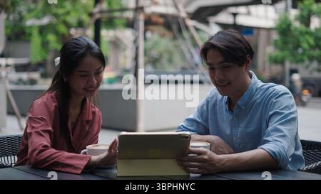 Two young professionals are using a tablet and drinking coffee at an outdoor cafe Stock Photo