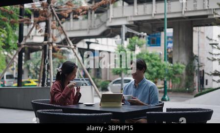 Two business colleagues are having a meeting at an outdoor cafe, drinking coffee and using a tablet Stock Photo