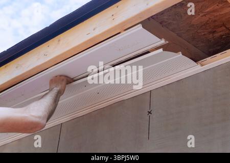 Worker is carefully placing new soffit siding panels under eaves of house Stock Photo