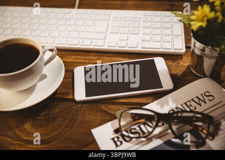 Flat design wooden desk is featuring centered smartphone, keyboard, coffee cup, newspaper, flowers Stock Photo