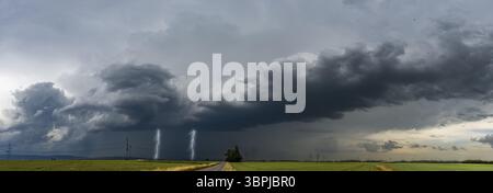 Panoramic view of a severe storm moving across the country with a grey, overcast sky, lightning and fields in the foreground Stock Photo