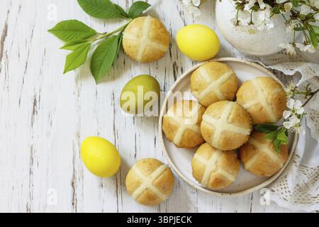 Happy Easter festive food concept. Homemade Easter traditional hot cross buns with raisin and natural colorful easter eggs on a rustic table. Top view Stock Photo