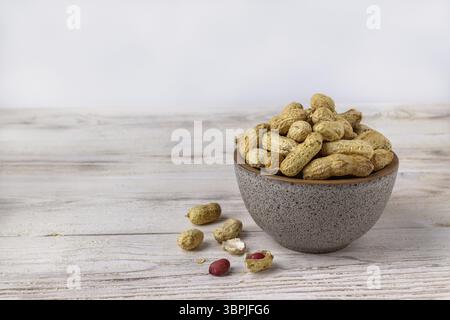 Peanuts lie in a clay cup on a white wooden table Stock Photo