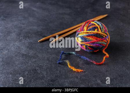 A ball of colorful threads and wooden knitting needles on a dark background, copy space Stock Photo