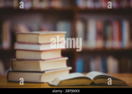 flat design is showing stack of hardcover books, open book on wooden table before blurred bookshelf Stock Photo