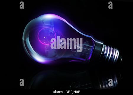 Single incandescent bulb is glowing with neon purple-blue filament on reflective table in 3D render Stock Photo