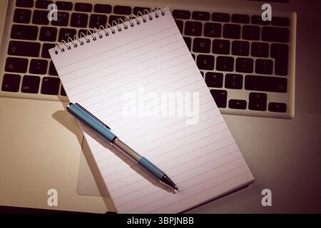 spiral-bound notebook with blue-silver ballpoint pen is resting on laptop keys in flat illustration Stock Photo
