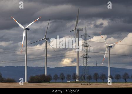 Wind turbines of a wind power plant in a condensed telephoto shot with mountains on the horizon and closed, grey cloud cover Stock Photo