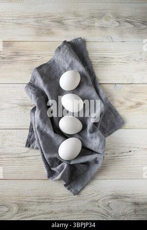 White chicken eggs lie on a gray napkin on a white wooden table Stock Photo