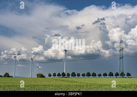 An approaching thunderstorm passes over the countryside with a wind farm on the horizon, a power line or high-voltage line with electricity pylons and Stock Photo