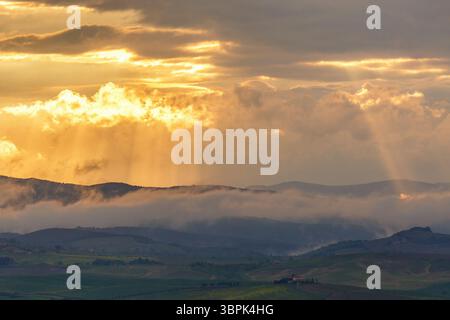 Sunset over the mountains with sun rays and low clouds Stock Photo