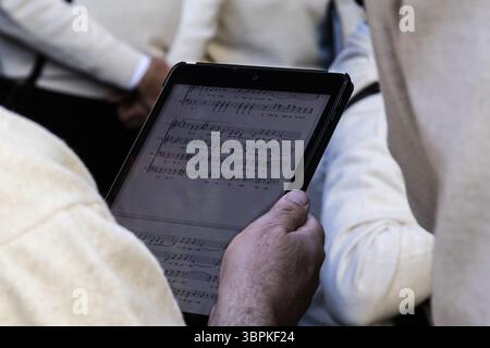 Close up of a musician's hand holding a digital tablet displaying a music score, suggesting the integration of technology in musical performances Stock Photo