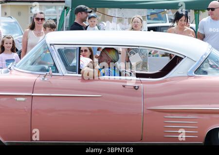 A man dresses as a hippy from the 60s drive-in a luxury 1954/1955 pink Cadillac car at a vintage car show in Essex UK Stock Photo