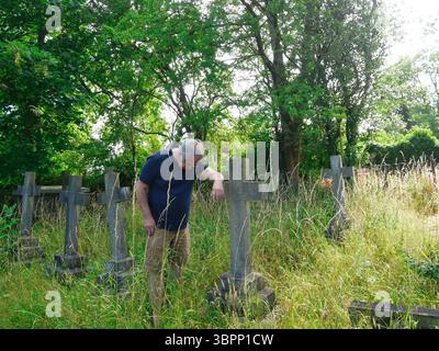 An elderly man with head bowed leaning on a grave stone in memory of a loved one Stock Photo