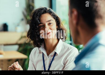Two young coworkers chatting over healthy lunch in bright office cafeteria Stock Photo