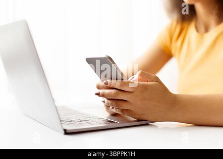 Closeup of female hands holding smartphone in front of laptop Stock Photo