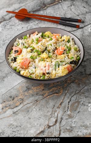 Stir fry rice with salmon, egg, green peas, onion and seaweed close-up in bowl on table. Vertical Stock Photo