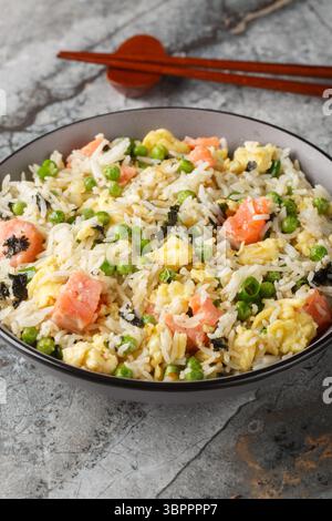 Fried rice with vegetables, salmon, egg and seaweed close-up in bowl on table. Vertical Stock Photo
