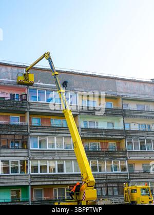 Workers on Boom Lift Repair Facade of Residential Apartment Building Under Clear Blue Sky Stock Photo