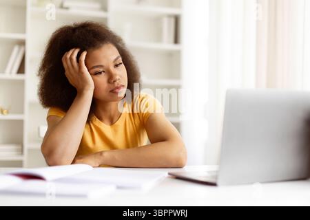 Bored young black woman resting head on hand while staring at laptop Stock Photo
