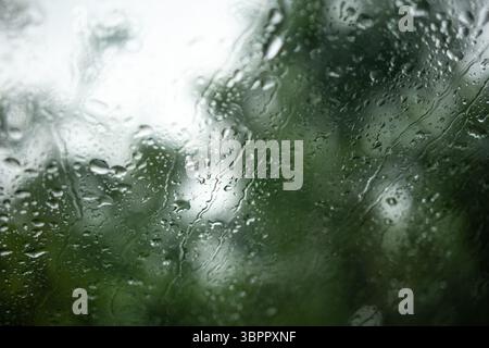 Raindrops on a car's windshield or windscreen. Inside looking out, wide angle shot, nature bokeh background, no people Stock Photo