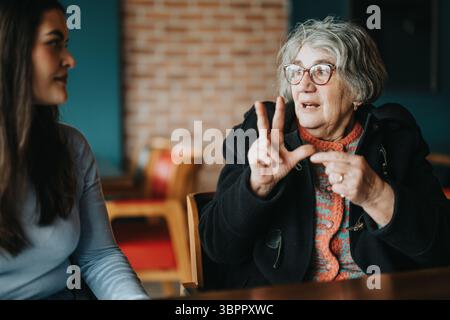 Senior woman communicating actively while seated indoors with another woman Stock Photo