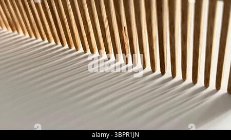 Close up image of a wooden comb resting on a white surface with dramatic shadows cast by natural light. The composition emphasizes the texture and pat Stock Photo