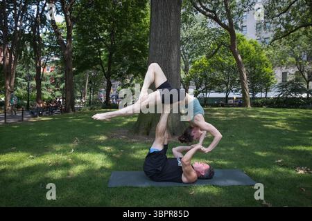 A graceful attractive lady performs Acroyoga, a practice that combines acrobatics & yoga. In Washington Square Park, Greenwich Village, Manhattan, NY. Stock Photo