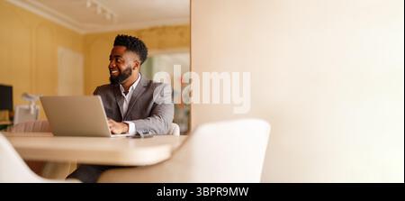 Smiling young businessman looking away confidently while working over wireless computer at desk in office Stock Photo