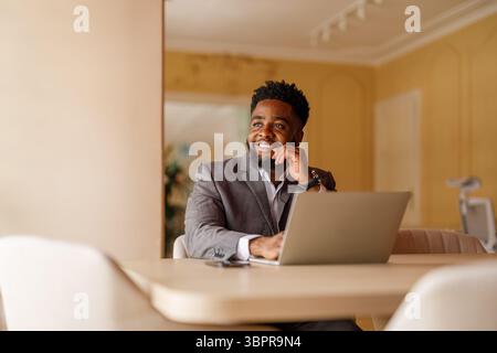 Thoughtful young businessman looking away while working online over laptop at desk in modern office Stock Photo