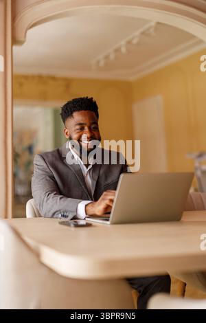 Portrait of smiling young businessman doing online research over laptop while sitting at desk in office Stock Photo