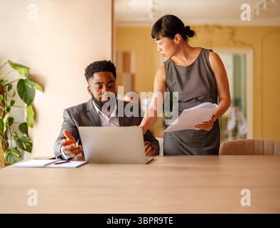 Serious financial professionals analyzing reports over laptop while working together at office desk Stock Photo