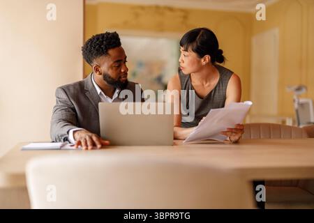 Focused business professionals discussing project with documents and laptop and sharing ideas in office Stock Photo