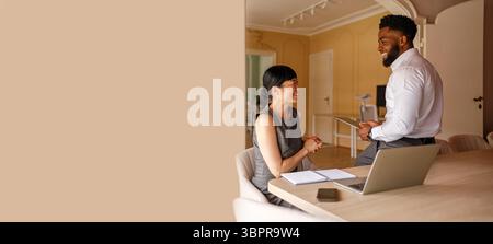 Smiling businessman using digital tablet while discussing with female colleague taking notes beside laptop at desk in office Stock Photo