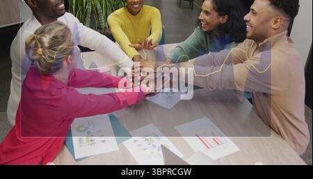 Colleagues wearing tops stacking hands in office meeting room, with laptop charts and graphs Stock Photo