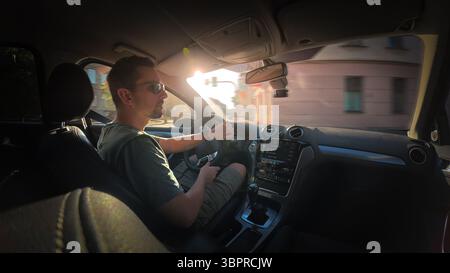Man driving a car with sunglasses on a sunny day, inside view with focus on dashboard and surroundings. Stock Photo