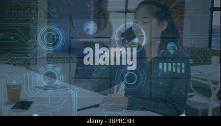 Asian businesswoman holding smartphone and writing in notebook at office table, with coffee cup Stock Photo