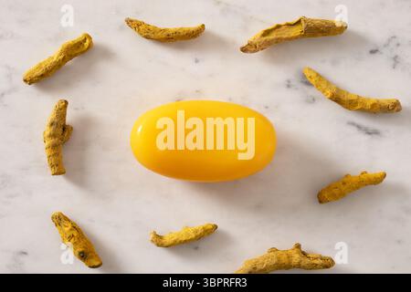 Turmeric soap bar and powder turmeric root on marble white background. Organic skincare product perfect for wellness, beauty, and organic body care co Stock Photo