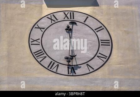 A close-up view of a large clock face mounted on a wall. The clock features Roman numerals and a simple design with two clock hands indicating the tim Stock Photo