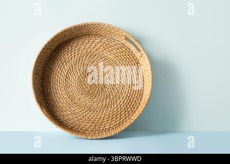 Round woven wicker basket, tray or plate stand on blue background. Handmade by local craftsmen in sri lanka traditional tableware. Stock Photo